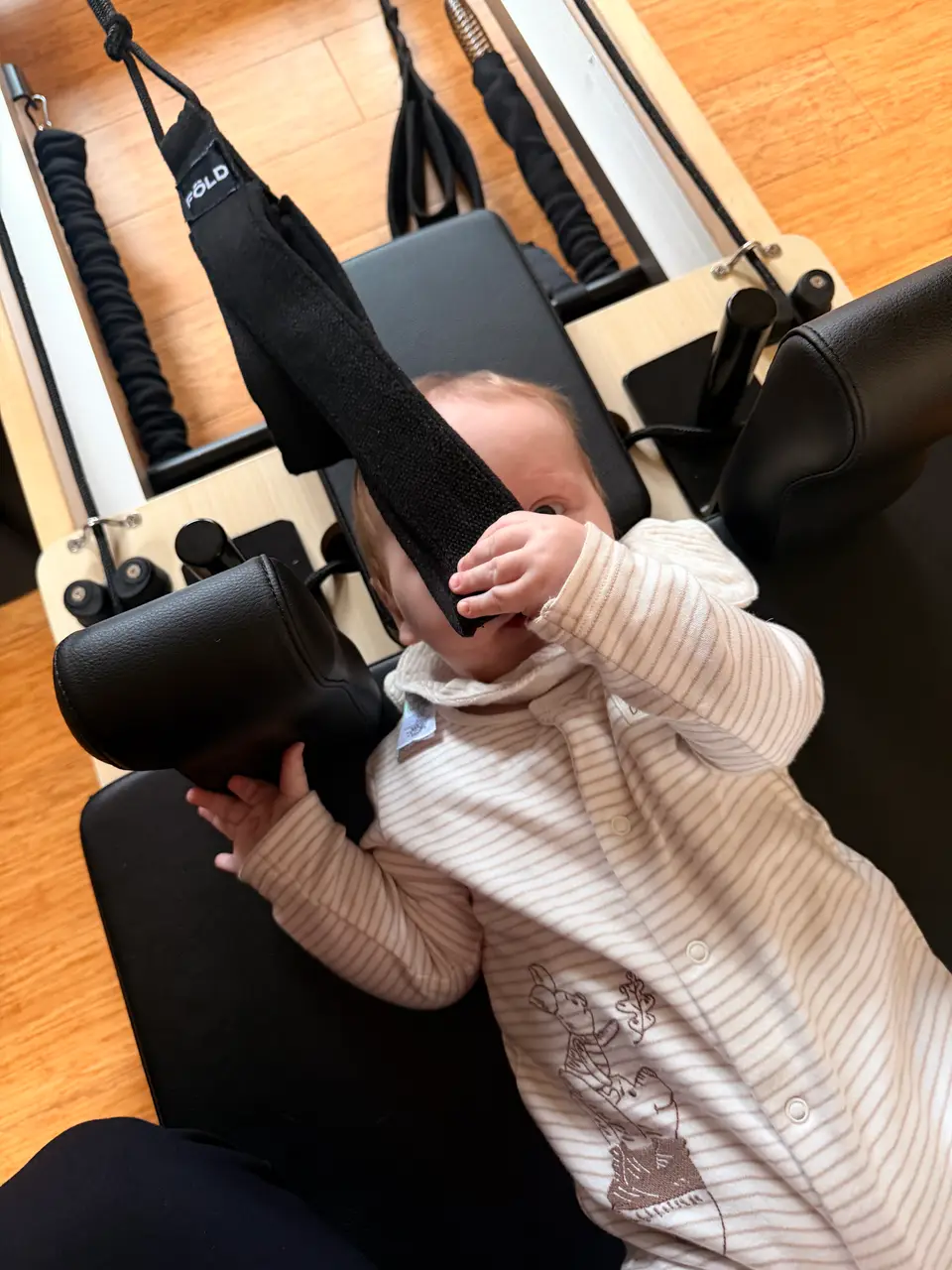 A baby lying on a reformer, holding one of its straps